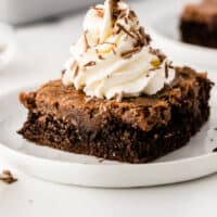 slice of triple chocolate gooey cake on a plate topped with whipped cream and chocolate shaving with recipe name at bottom