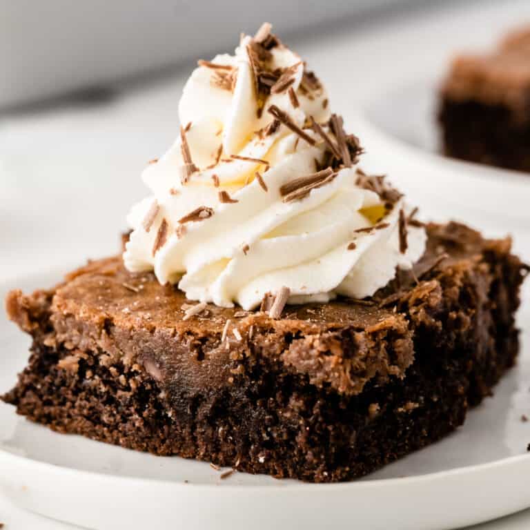 square image of a slice of triple chocolate gooey cake topped with whipped cream