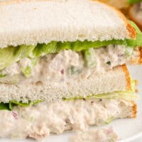 image of two tuna salad sandwich halves stacked on a plate with potato chips with the title of the post on top in pink and black lettering