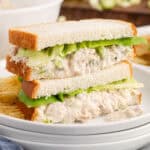 square image of two tuna salad sandwich halves stacked on a plate with potato chips