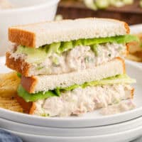 square image of two tuna salad sandwich halves stacked on a plate with potato chips