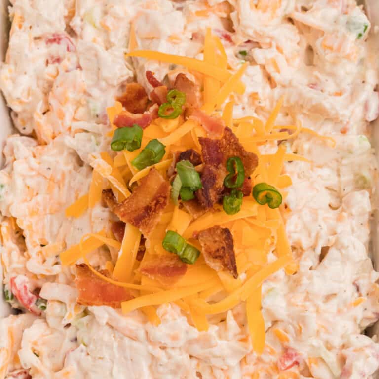 square close up of ultimate loaded garlic chicken dip with cheese bacon and green onion on top
