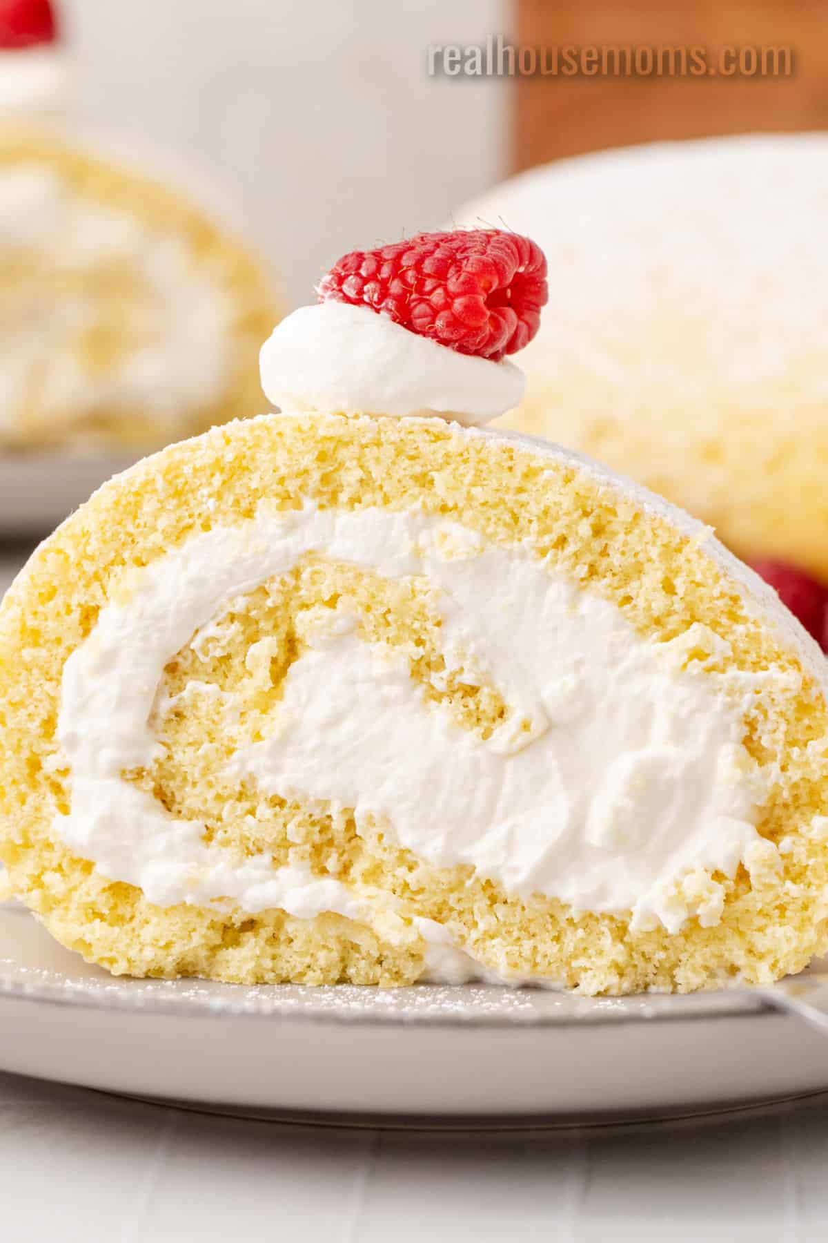 close up of a slice of vanilla swiss roll topped with whipped cream and a raspberry