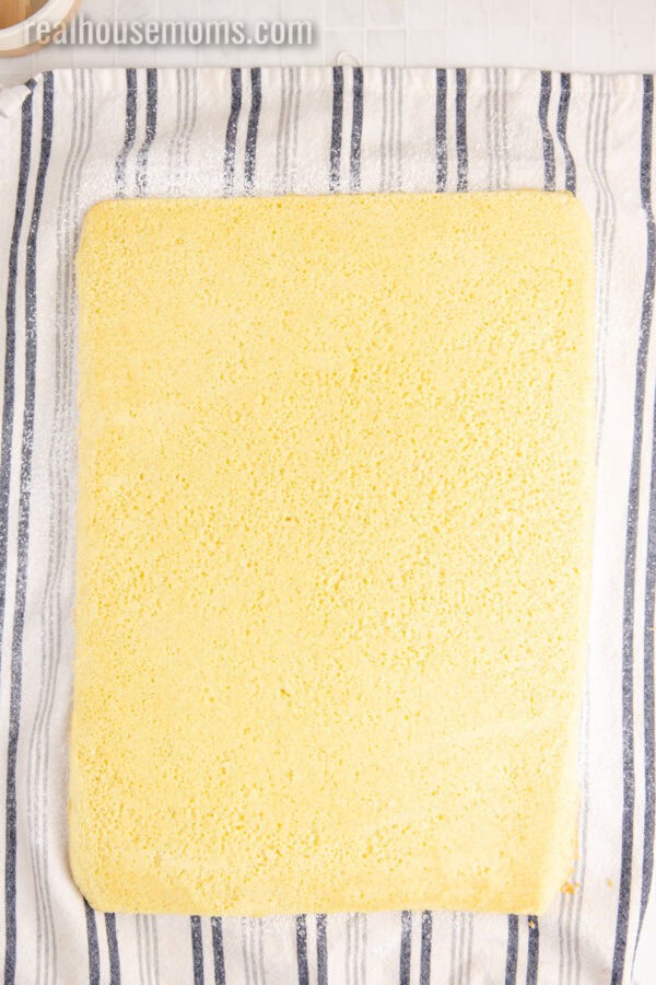 baked vanilla swiss roll cake on a tea towel coated in powdered sugar