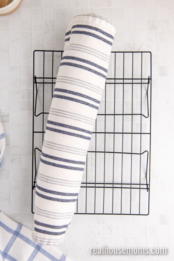 vanilla swiss roll rolled up in a tea towel on a wire rack