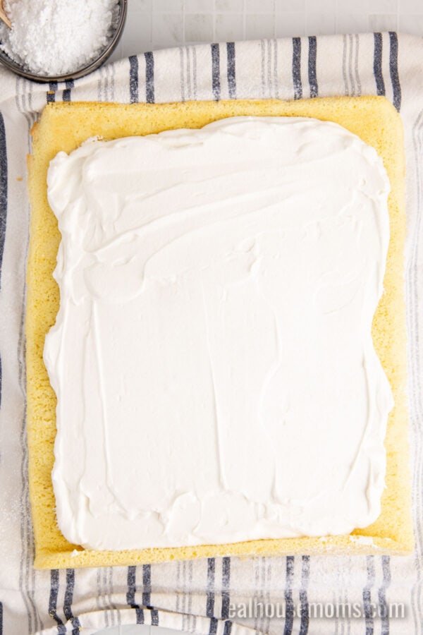 chantilly cream spread over a vanilla swiss roll cake