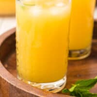 glasses of virgin orange mango mojito on a wooden tray with recipe name at the bottom