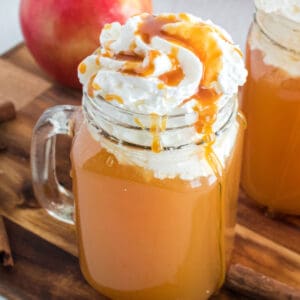 square image of warm apple cider in a mug with whipped cream and caramel on top