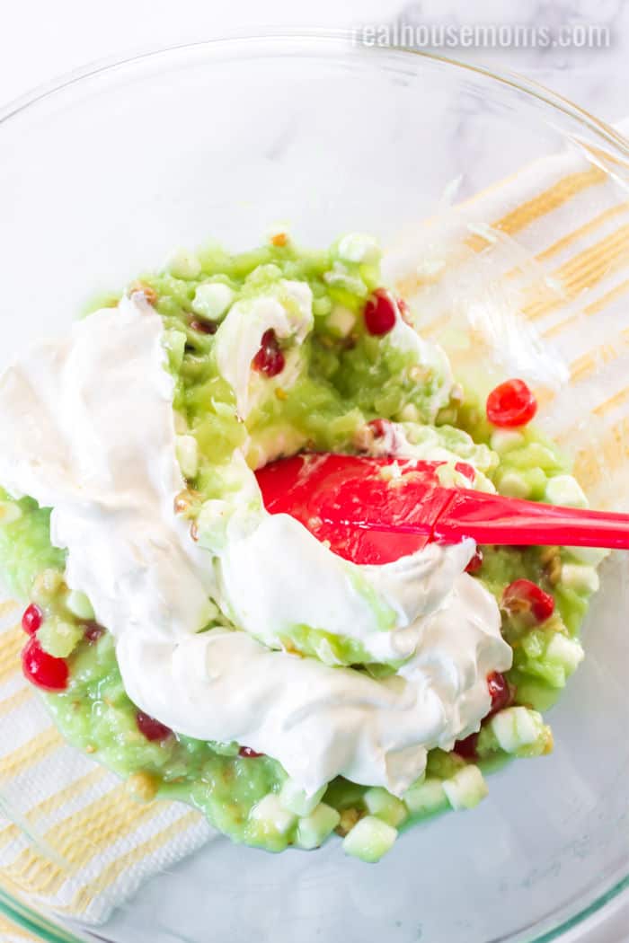 whipped topping being folded into pistachio pudding with fruit and nuts