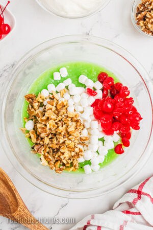 chopped walnuts, mini marshmallows, and chopped cherries added to a mixing bowl with pistachio pineapple mixture