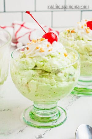 side view of watergate salad in a dessert dish topped with whipped cream, chopped nuts, and a cherry