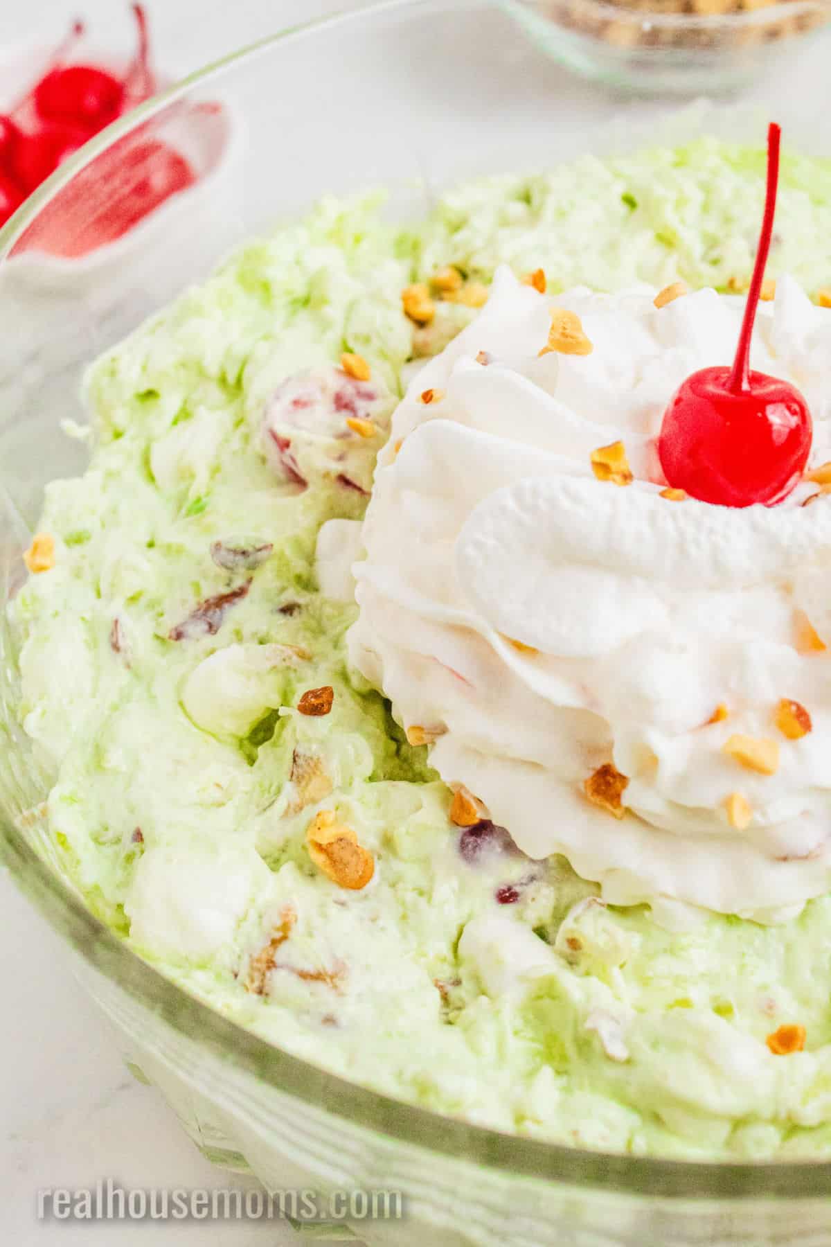 serving bowl of watergate salad topped with whipped topping and a cherry