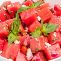 square close up of watermelon salad in a bowl with basil sprigs