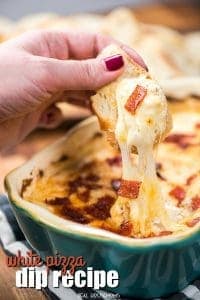 Bread lifting out of a pan of white pizza dip with gooey cheese pulling away