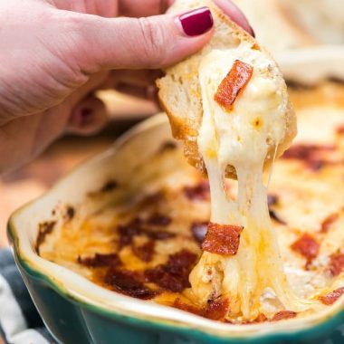 Bread lifting out of a pan of white pizza dip with gooey cheese pulling away