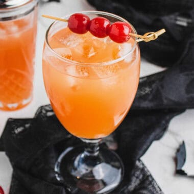 square image of witch's brew cocktail in a glass with maraschino cherries for garnish