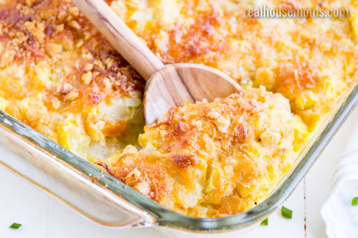 spoonful of yellow squash casserole being taken from the baking dish