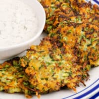 square image of zucchini fritters on a plate next to a bowl of greek yogurt ranch dressing