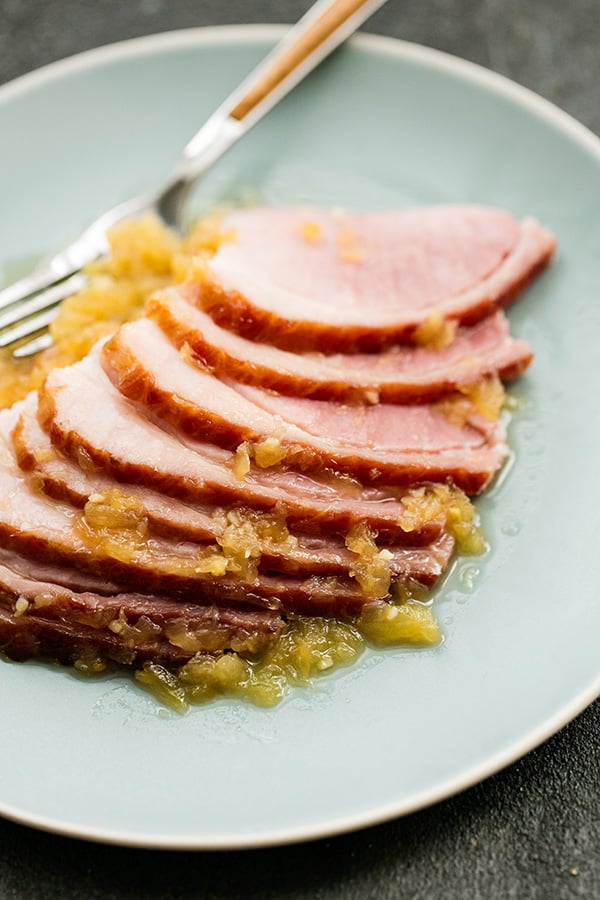 Pineapple Glazed Ham slices served on a plate with a fork and extra glazed drizzled over the top