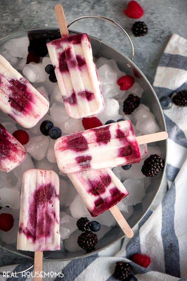 Overhead shot of Berries & Cream Popsicles laying flat on a tray filled with ice cubes and berries