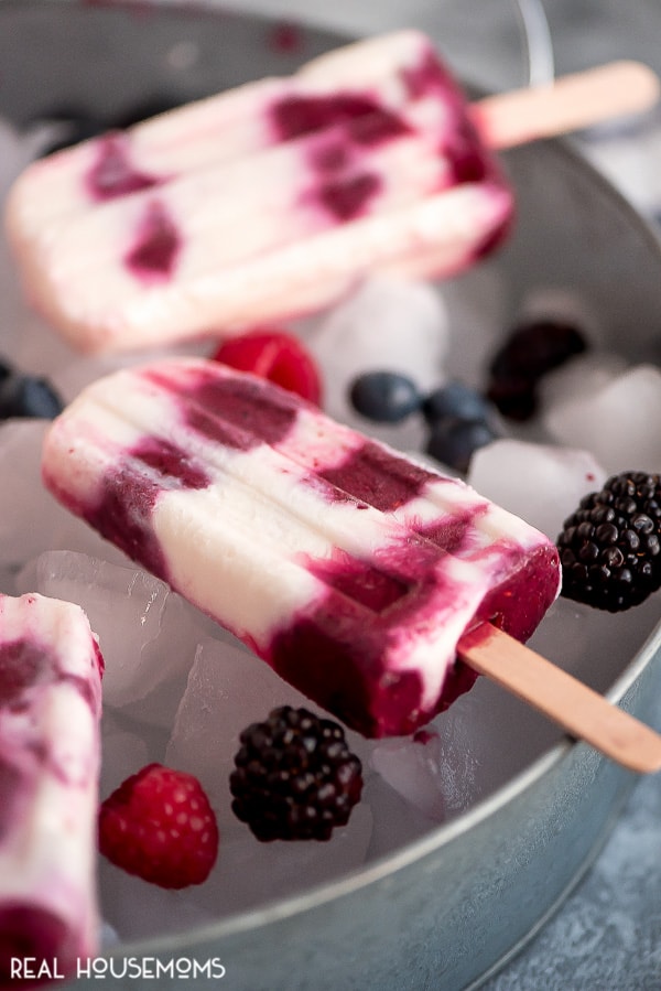 Berries & Cream Popsicles laying on top of a tray filled with ice and berries