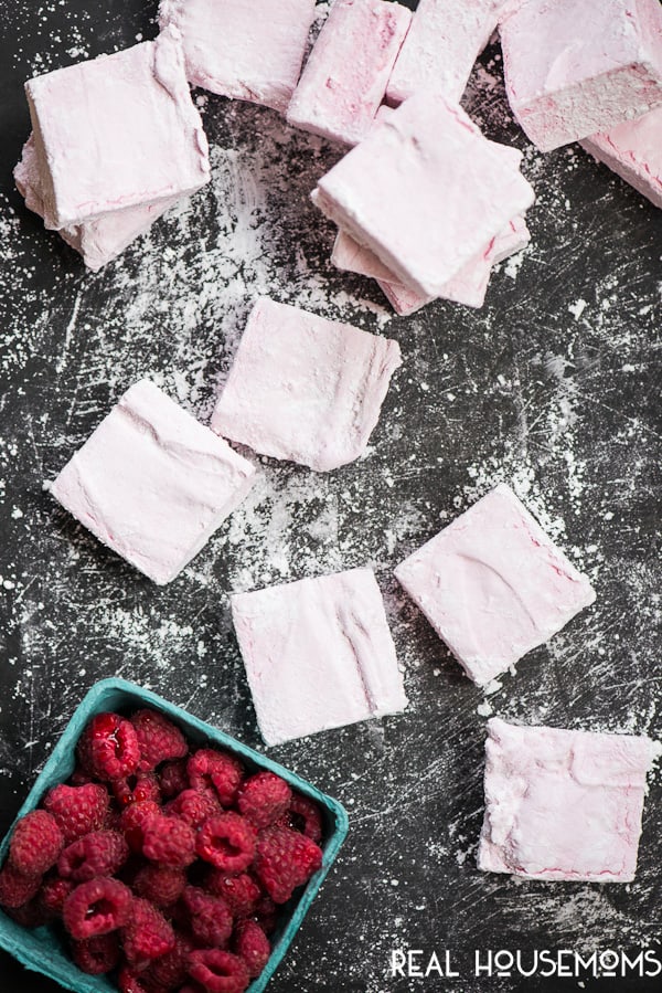 Homemade Raspberry Marshmallows cut up and strewn over a counter next to a basket of raspberries